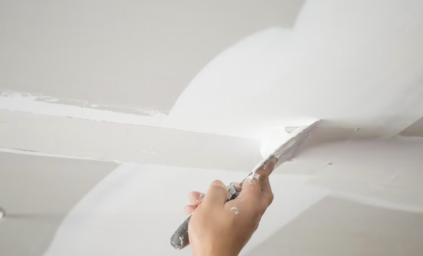 Taping knife floating a seam smooth against the ceiling line