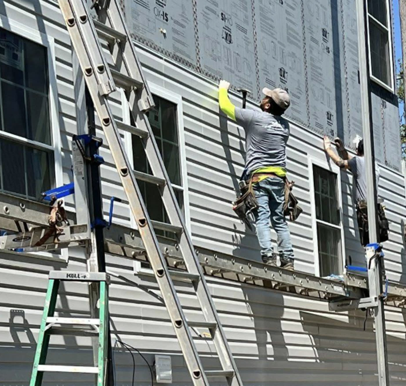Crew on a plank working siding back over the house wrap